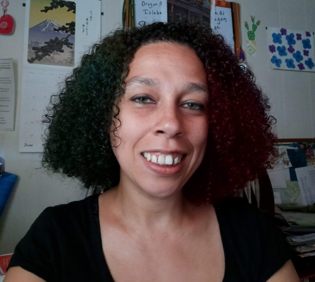 Headshot of workshop facilitator, woman with tanned skin and dark curly.