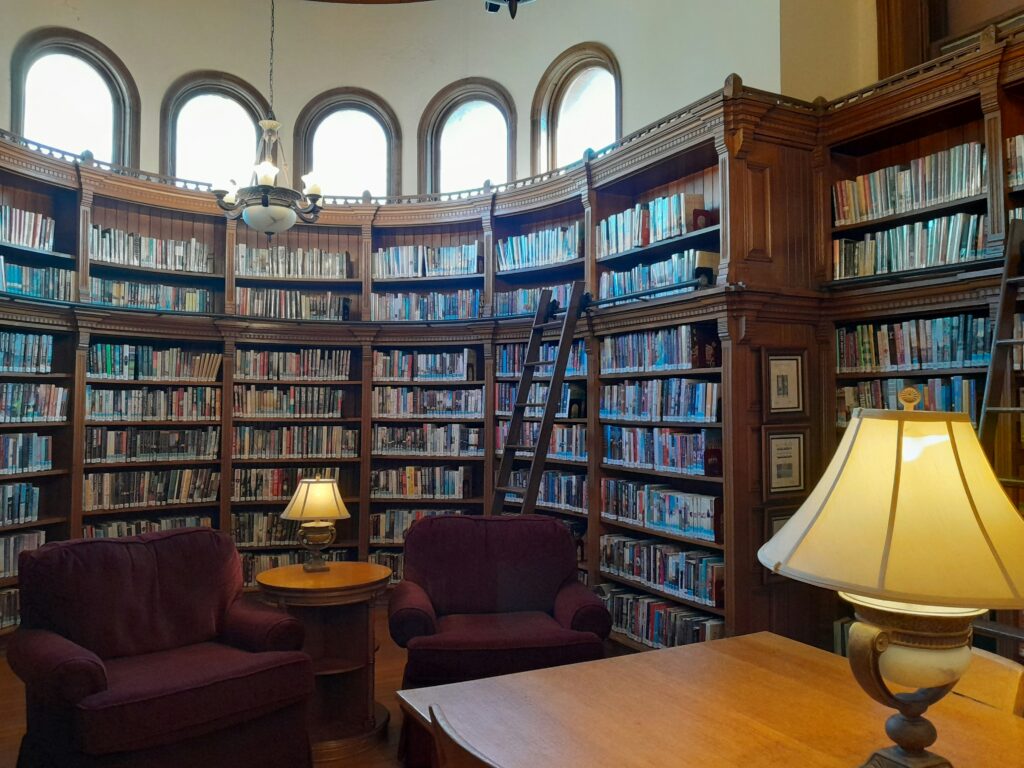 Interior of library with two large armchairs facing a table with lamp. 