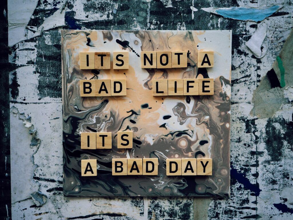 Tiles spelling out It's not a bad life its a bad day, on canvas with black, white and beige colors swirled around.